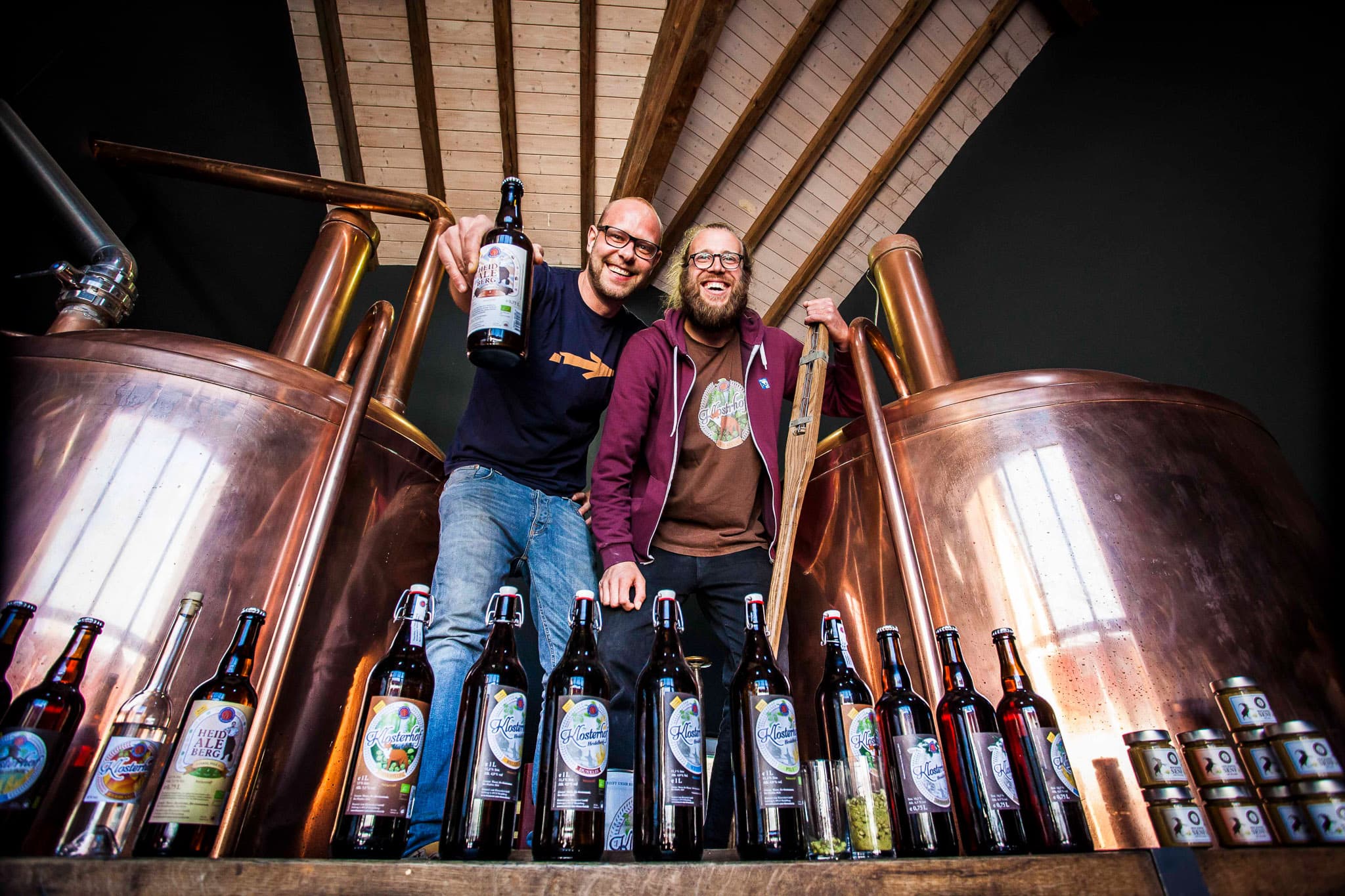 Business portrait of two men in front of a beer brewery business setting holding their product beer bottles in hand 